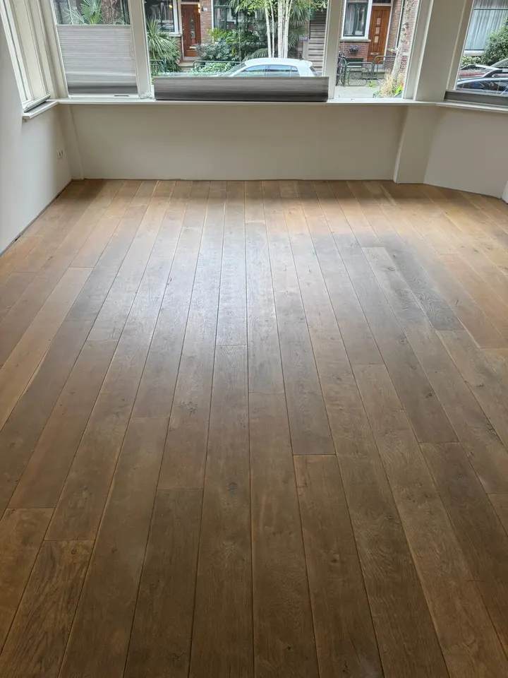Brede eiken planken in een kamer met erker, donker en dof met een versleten, vlekkerig oppervlak