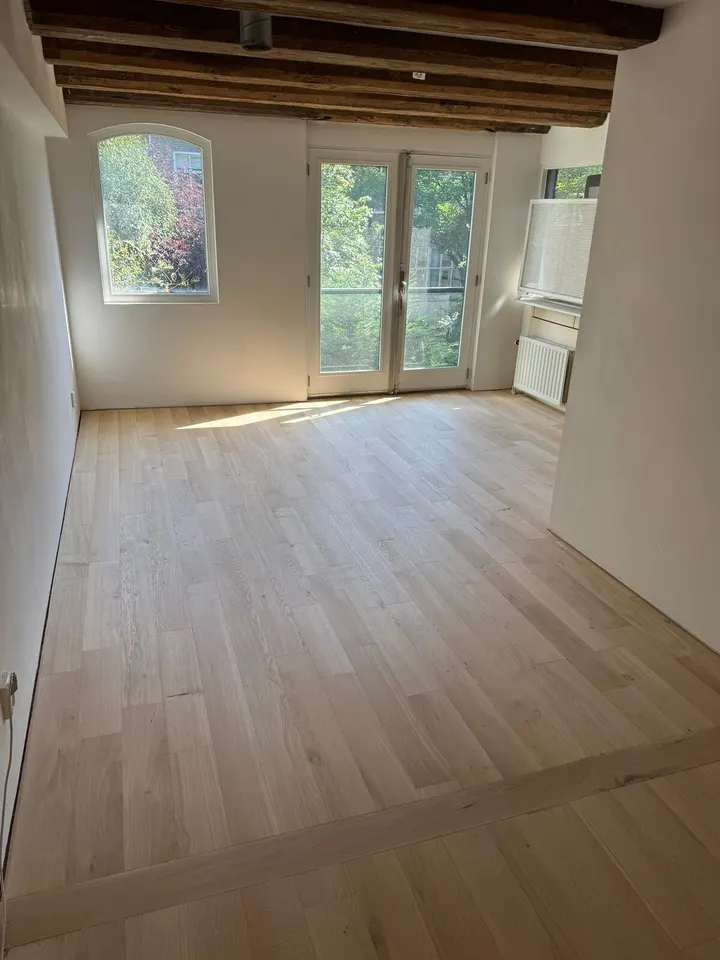 Dezelfde kamer met balken van verder weg, de lichte eiken vloer doorlopend tot openslaande deuren