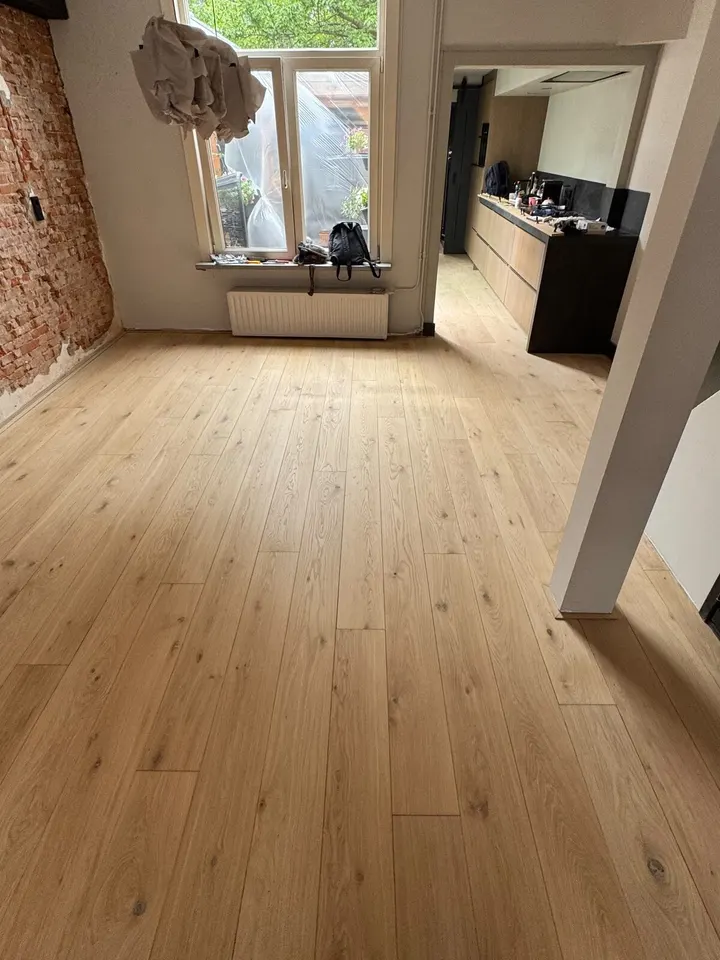 De geschuurde eiken plankenvloer langs de bakstenen muur, doorlopend naar een open keuken