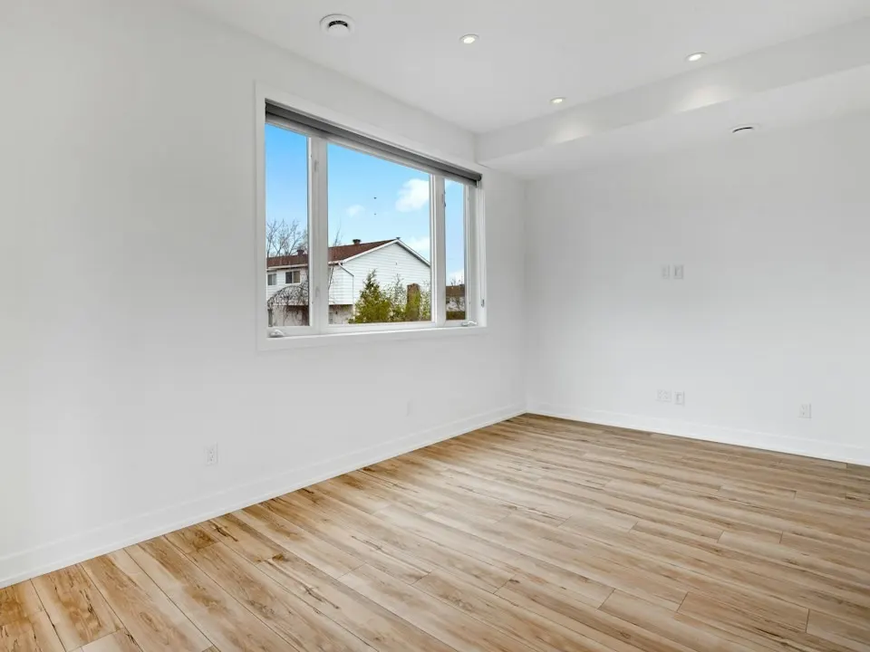 Een lege kamer met een houten vloer en een raam