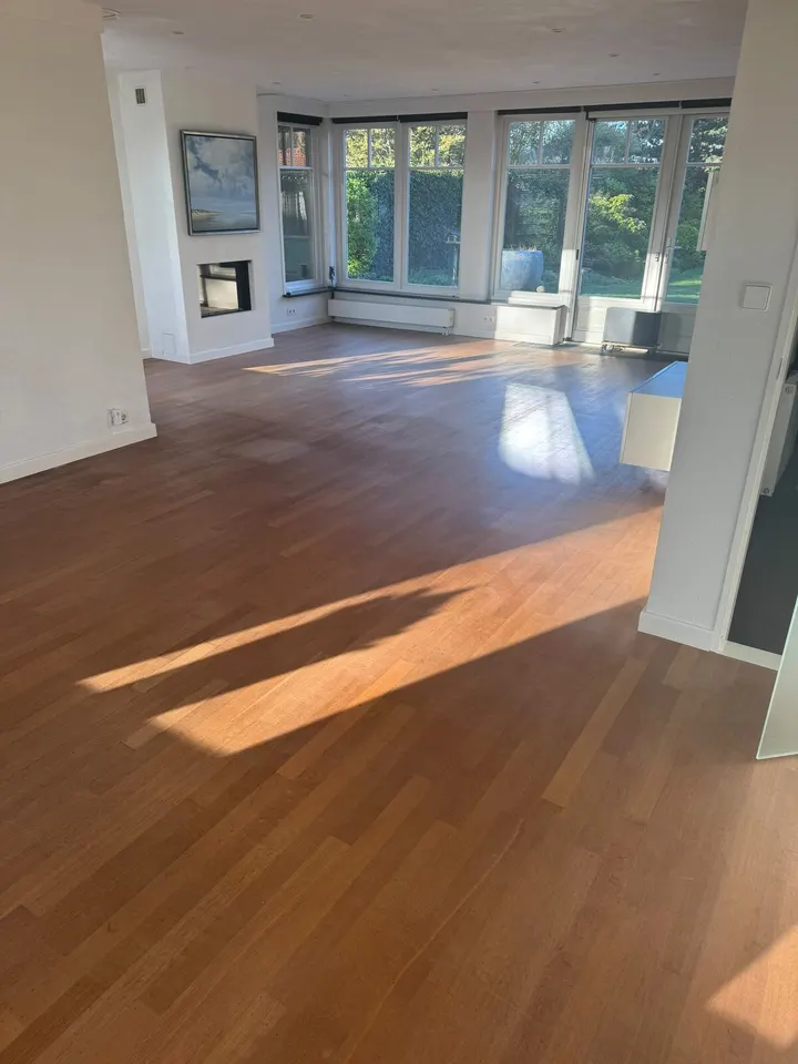 Strokenvloer in een grote kamer met open haard en hoge tuinramen, de afwerking plaatselijk glimmend