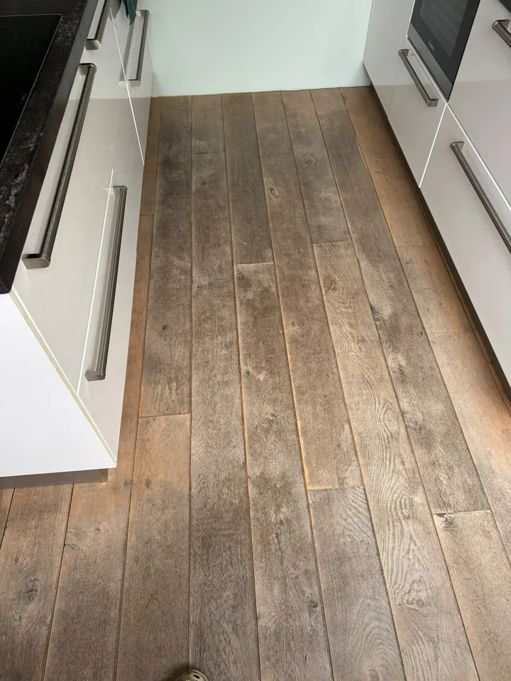 Smalle keuken met witte kasten en brede eiken planken, grijs en versleten, voor het schuren