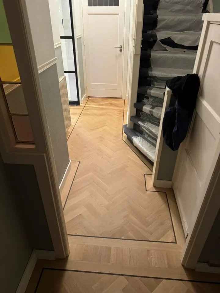 Visgraatparket in de hal, omlijst door een smalle donkere bies die de muren en de voet van de trap volgt