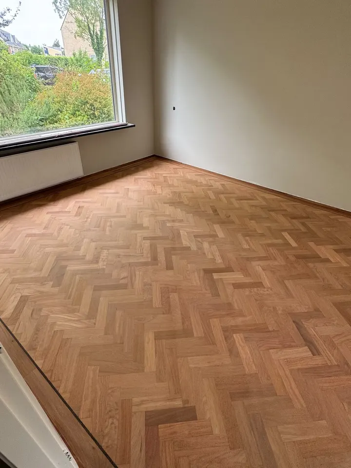 Dezelfde visgraatvloer teruggeschuurd tot kaal hout, licht en egaal, onder het tuinraam
