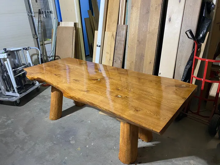 De afgewerkte eiken boomstamtafel met natuurlijke rand op ronde boomstampoten, geolied tot een diepe glans, in de werkplaats