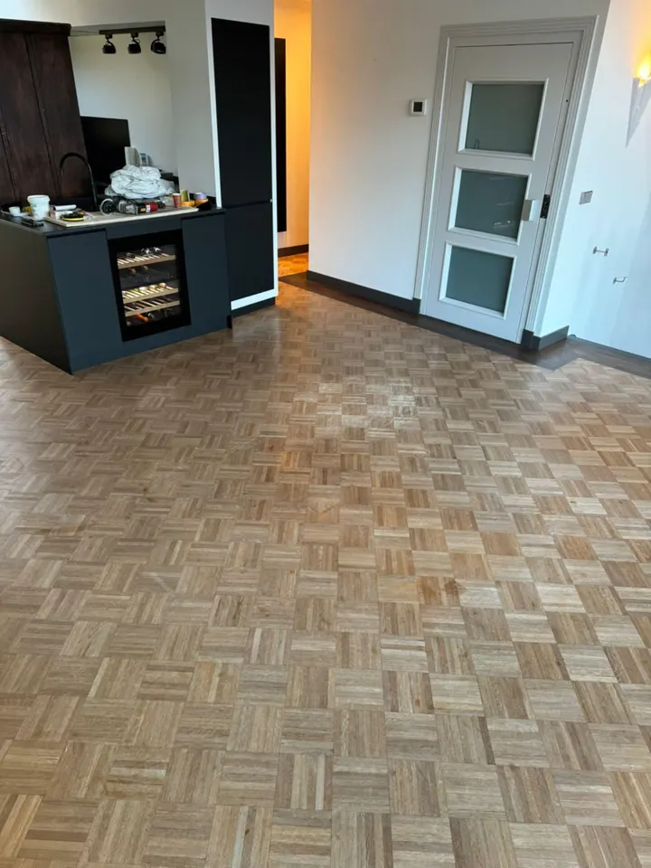 Dezelfde kamer met het eiken mozaïekparket teruggeschuurd tot kaal, licht hout