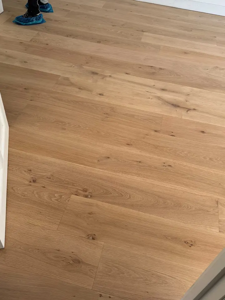 Eiken plankenvloer met noesten bij een open witte deur, de overschoenen van een vakman net in beeld