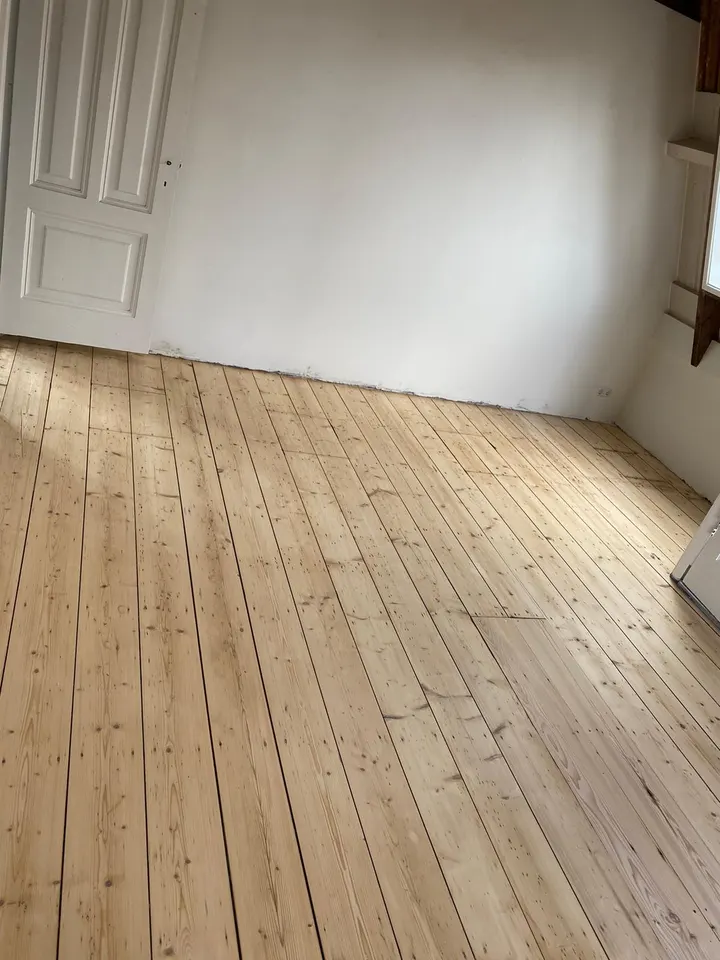 Geschuurde grenen vloerdelen over de hele lengte van een lege kamer met witte muren