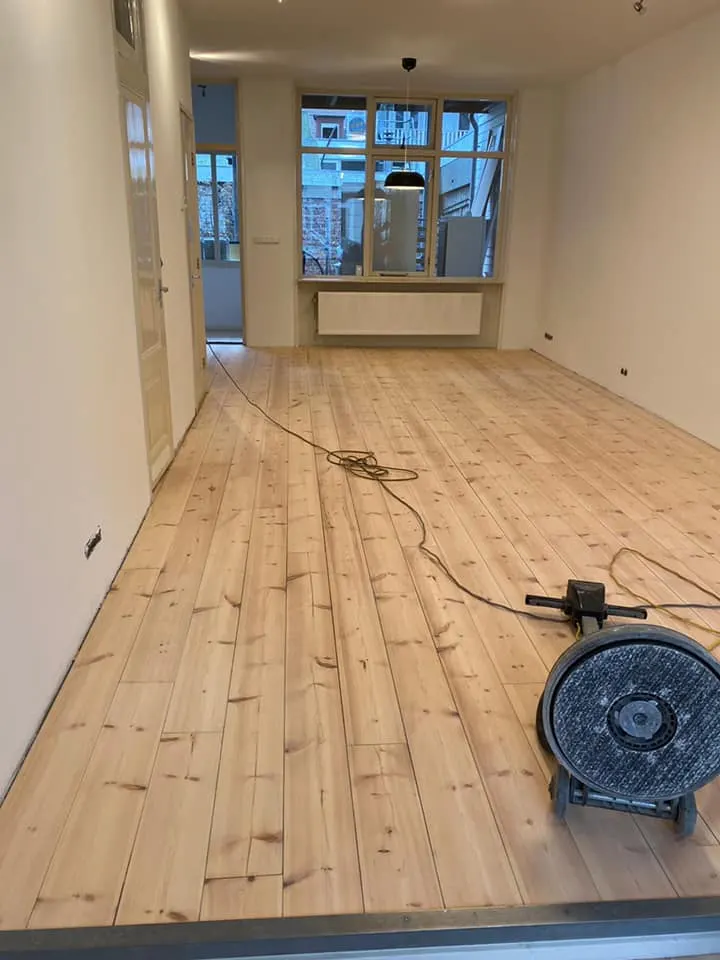 Een boenmachine op vers geschuurde grenen vloerdelen in een lange, smalle kamer