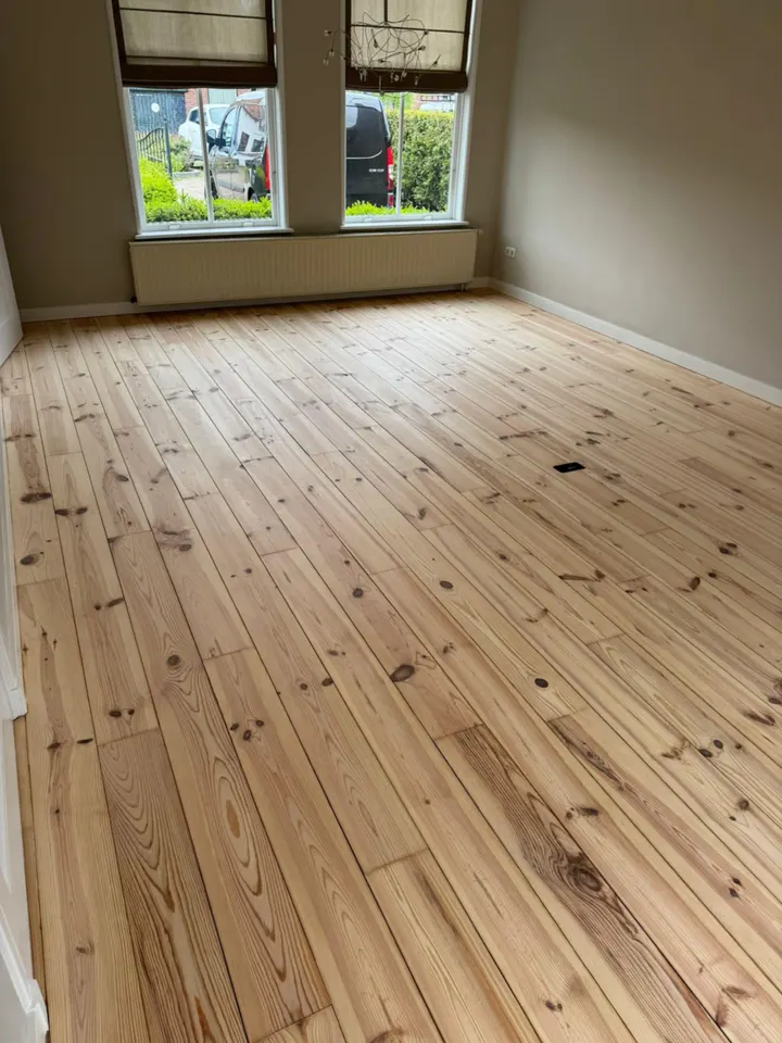 Grenen plankenvloer teruggeschuurd tot een natuurlijke lichte tint in een kamer met erker