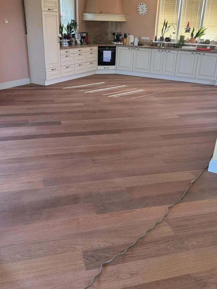 Open keuken met roze muren en een roodbruine plankenvloer, met een stroomkabel eroverheen