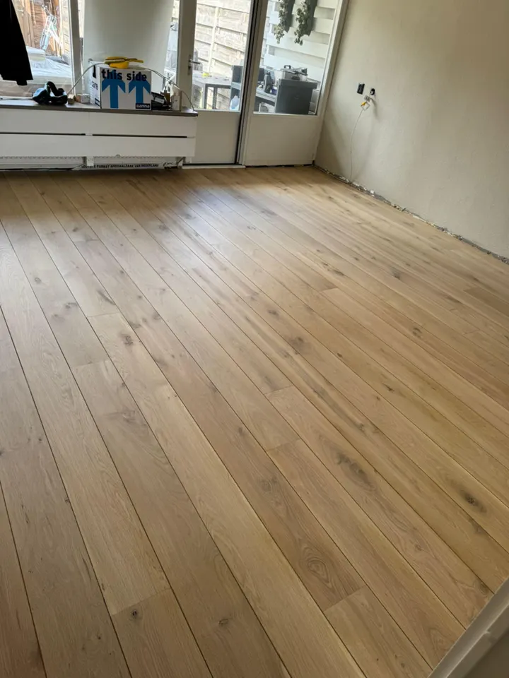 Een breder aanzicht van dezelfde licht eiken plankenvloer, vanuit de deuropening naar de tuindeuren