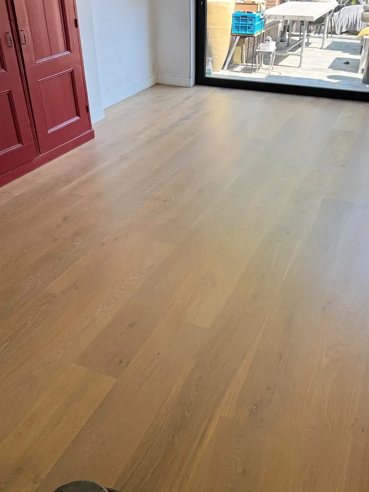 Dezelfde eiken vloer bij de rode kast na de behandeling, egaal en licht