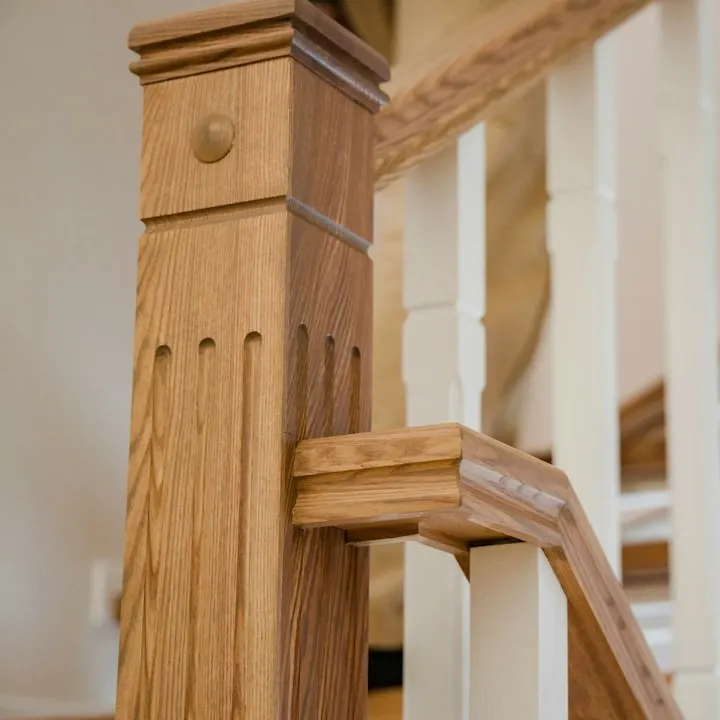 Detail van een eiken trappaal naast witte spijlen