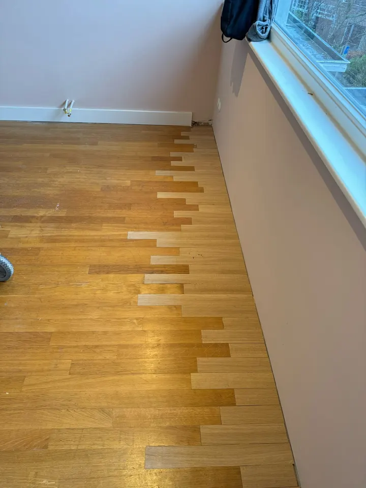 Lichte nieuwe eiken stroken ingelegd in een bestaande vergeelde strokenvloer langs een muur, de naden verspringend zodat beide in elkaar grijpen